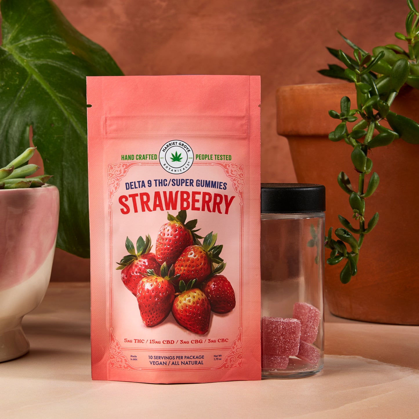 Pink package of strawberry-flavored gummies with a glass container on a neutral background