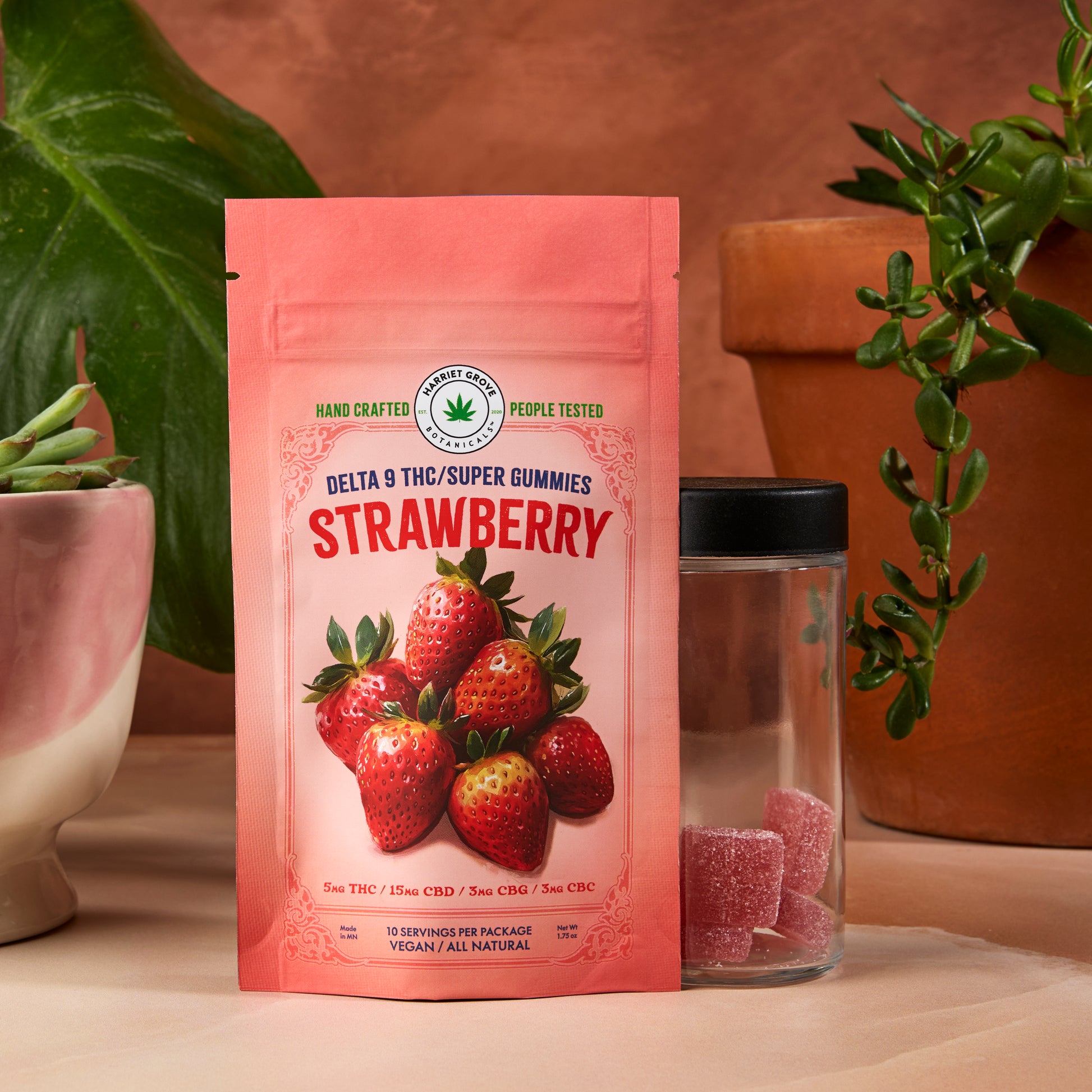 Pink package of strawberry-flavored gummies with a glass container on a neutral background